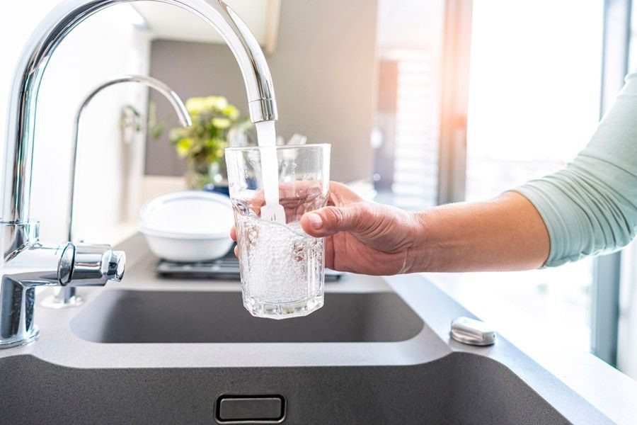 Person rinsing a tall glass under a running faucet in a modern kitchen sink